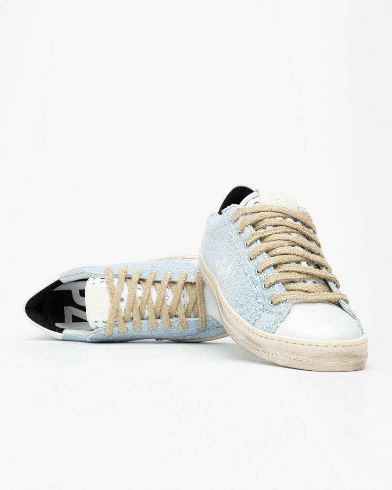 A pair of distressed denim lowtop sneakers, set against a bright white background.