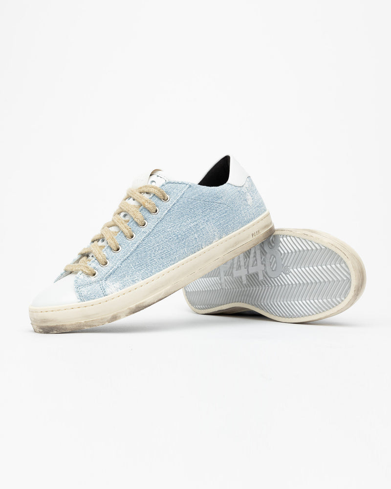 A pair of distressed denim lowtop sneakers, set against a bright white background.