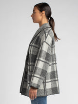 Side view of the model wearing a black and grey plaid jacket and a white rib top underneath and a pair of jeans.