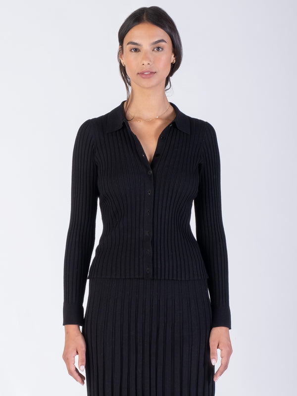 Model wearing a black ribbed fitted cardigan with a collar neckline and a color matching ribbed pleated skirt.