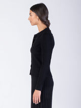 Side view of the model wearing a black ribbed fitted cardigan with a collar neckline and a color matching ribbed pleated skirt.