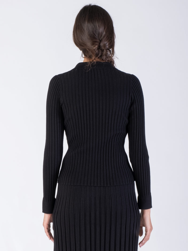 Back view of the model wearing a black ribbed fitted cardigan with a collar neckline and a color matching ribbed pleated skirt.