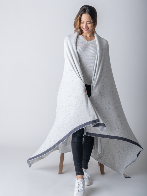 A woman standing, wearing a large, grey cotton blanket draped over her shoulders. 
