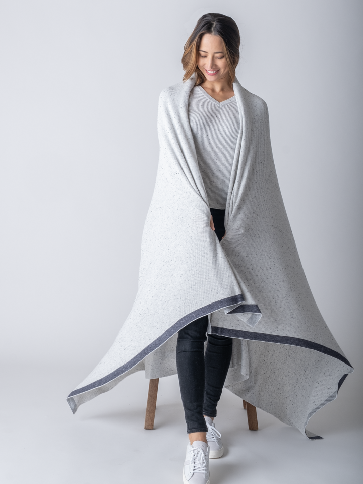 A woman standing, wearing a large, grey cotton blanket draped over her shoulders. 