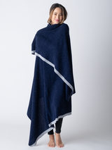 A woman standing, wearing a large, navy cotton blanket wrapped around her shoulders.