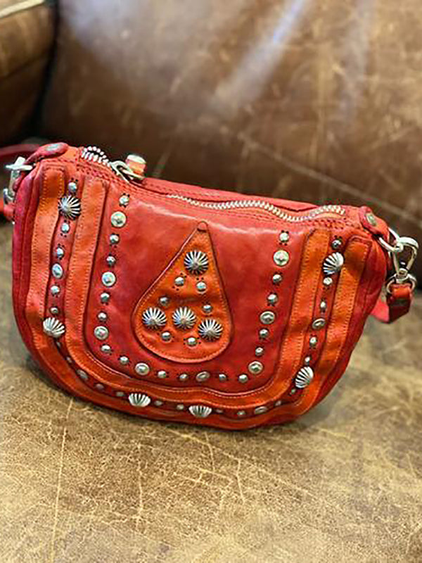 Red leather bag made with piece-dyed natural cowhide, laser-etched and ornate stud detailing and an adjustable/removable leather strap.
