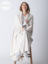 A woman sitting on a stool, wearing a large, white cotton blanket draped over her shoulders.