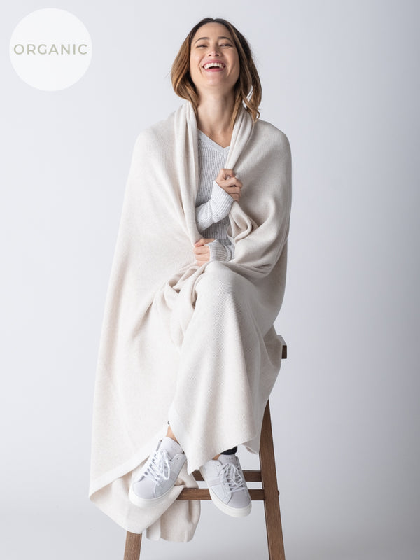 A woman sitting on a stool, wearing a large, white cotton blanket draped over her shoulders.