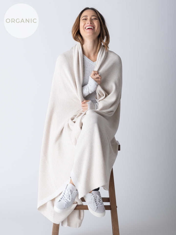 A woman sitting on a stool, wearing a large, white cotton blanket draped over her shoulders.