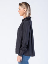 Side view of the model wearing a black blouse with a button closure and a pair of jeans.