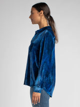 Side view of the model wearing a blue velvet shirt and a pair of jeans.
