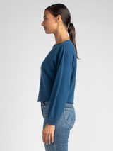 Side view of the model wearing a blue cropped pullover with a drop-shoulder silhouette and a pair of jeans.