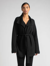 Model wearing a black two pockets jacket with a waist tie and a pair of pants.