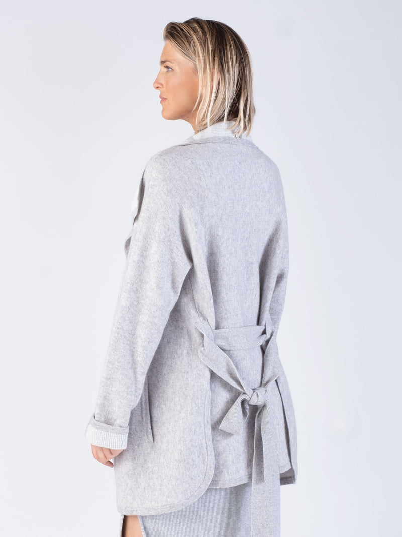 Back view of the model wearing a light grey two pockets jacket with a waist tie