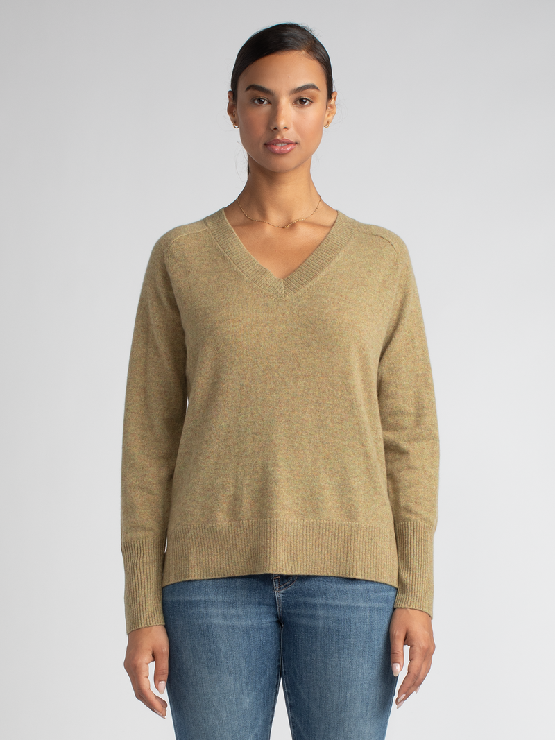 Model wearing a mustard yellow vee neck pullover with ribbed details at the hem, neckline and cuffs and a pair of jeans.