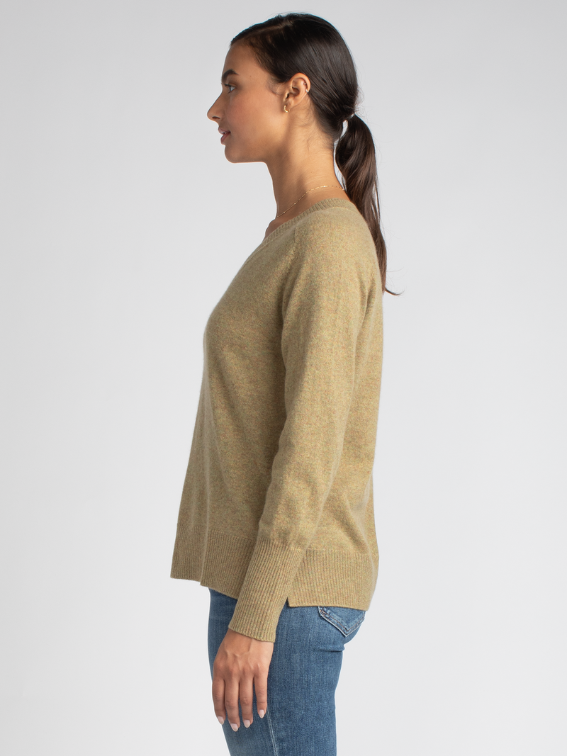 Side view of the model wearing a mustard yellow vee neck pullover with ribbed details at the hem, neckline and cuffs and a pair of jeans.