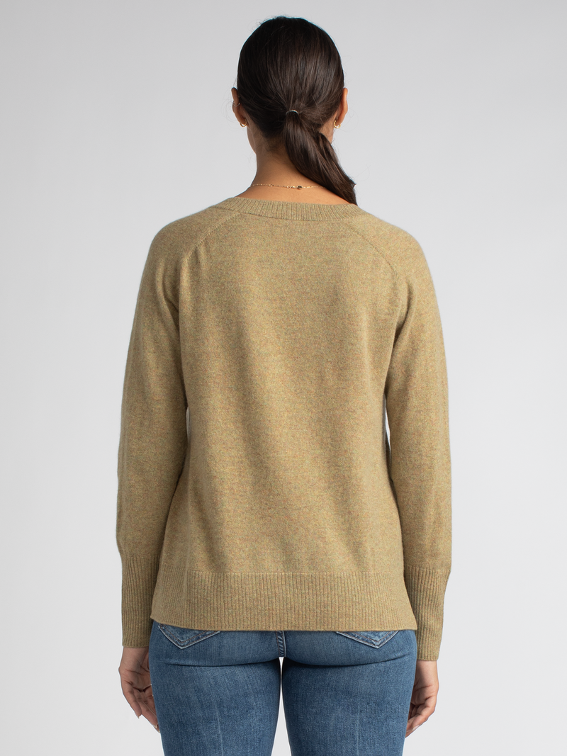 Back view of the model wearing a mustard yellow vee neck pullover with ribbed details at the hem, neckline and cuffs and a pair of jeans.