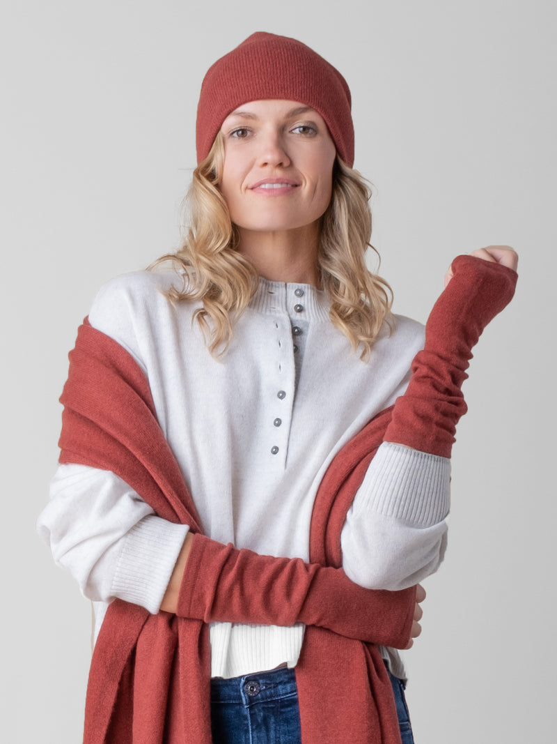 Model wearing a white pullover, a pair of rust texting gloves, a rust beanie and a rust wrap around her arm.