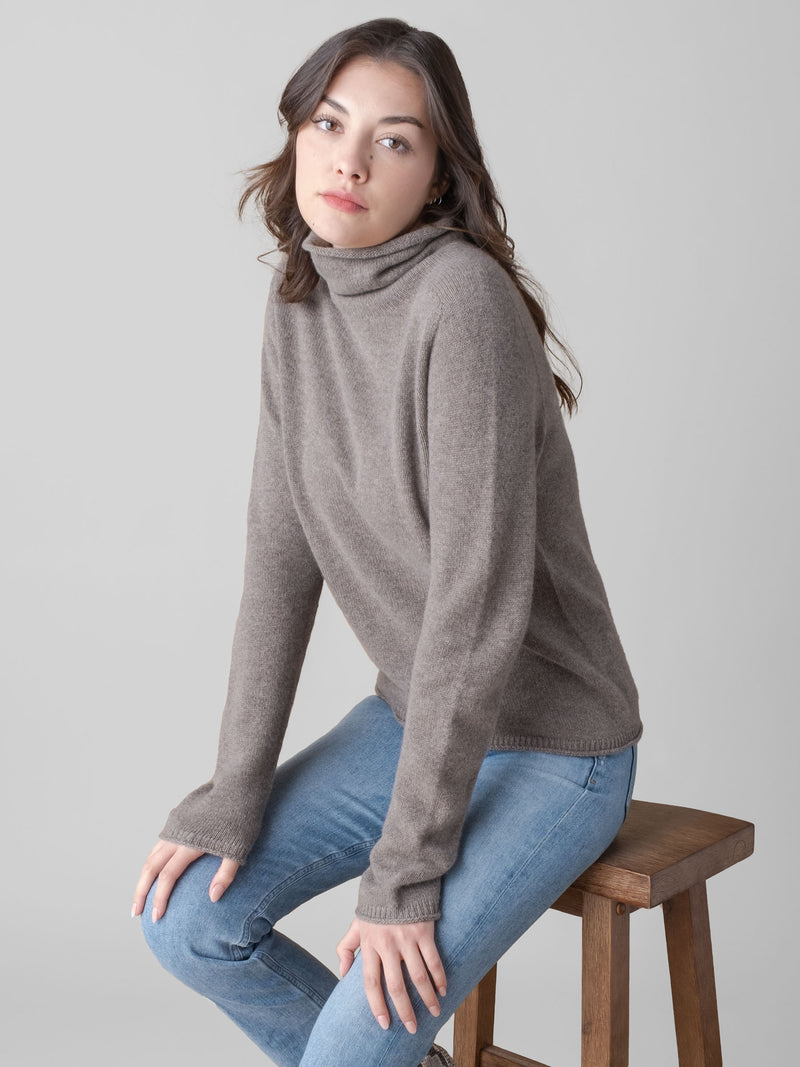 Model wearing a grain color turtleneck pullover and a pair of jeans.