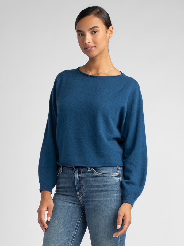 Model wears a blue cropped pullover with a drop-shoulder silhouette and a pair of jeans.