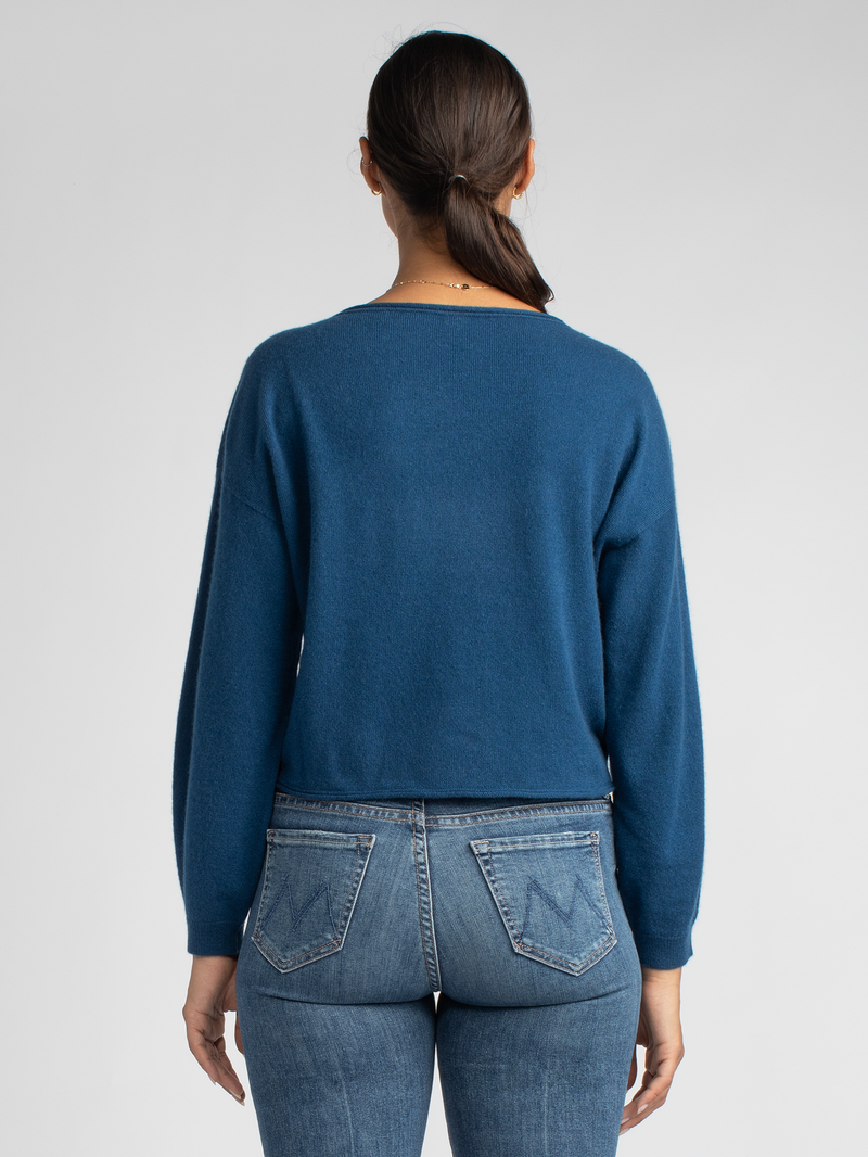 Back view of the model wearing a blue cropped pullover with a drop-shoulder silhouette and a pair of jeans.