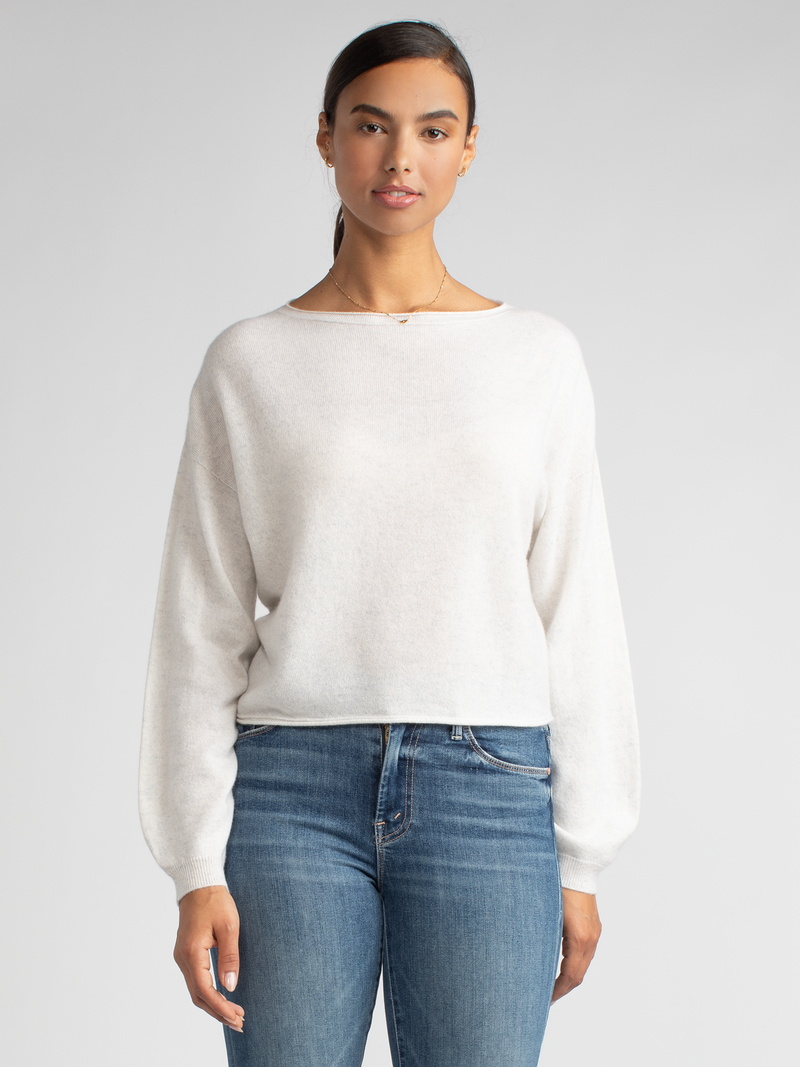 Model wearing a white cropped pullover with a drop-shoulder silhouette and a pair of jeans.