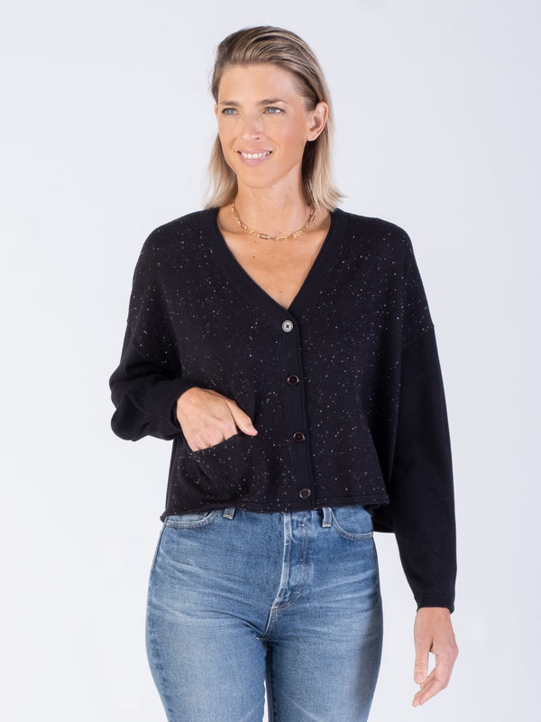 Front view of the model wearing a black flecks and black color cropped cardigan and a pair of jeans.