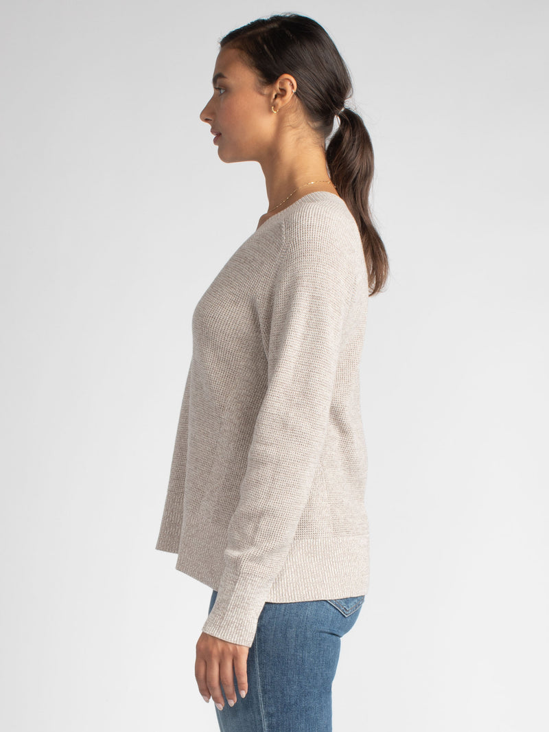 Side view of the model wearing a soy vneck pullover and a pair of jeans.