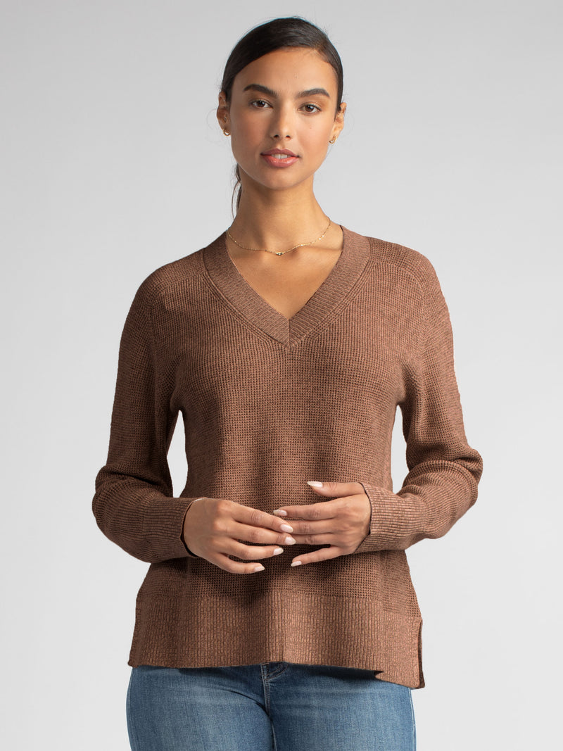 Front view of the model wearing a peanut vneck pullover and a pair of jeans.