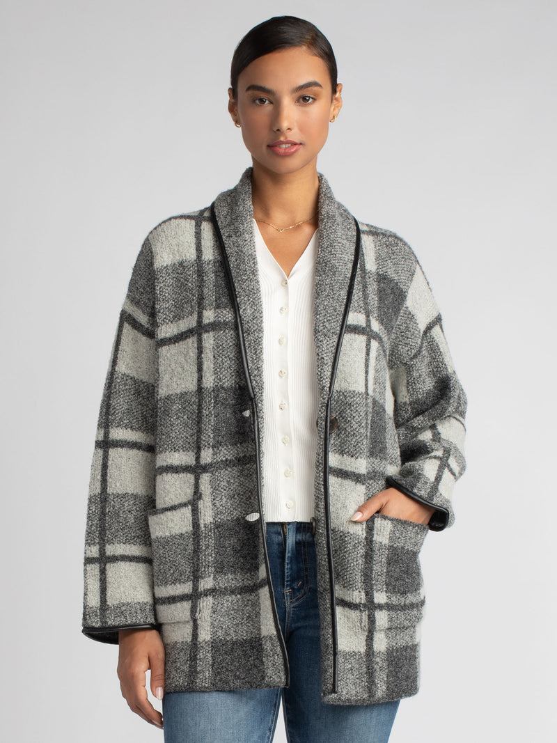 Model wearing a black and grey plaid jacket and a white rib top underneath and a pair of jeans.