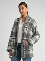 Model wearing a black and grey plaid jacket and a white rib top underneath and a pair of jeans.