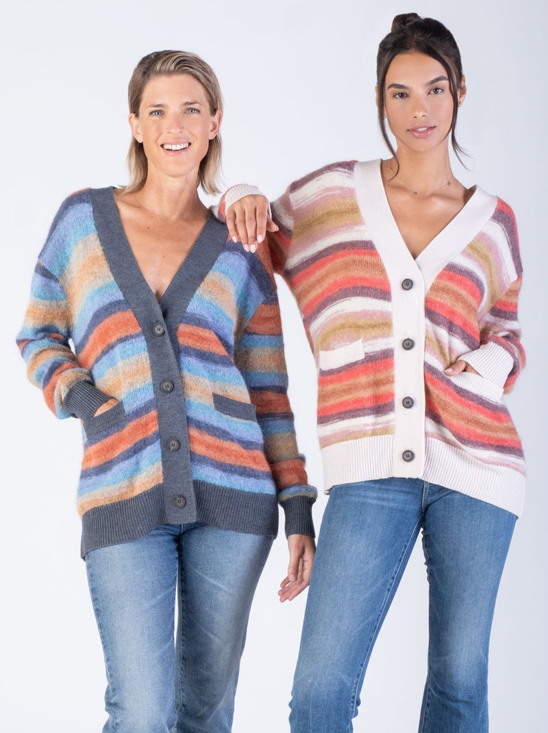 Model at the left wearing a grey, blue, purple, and orange striped cardigan and a pair of jeans; model at the right wearing a white, pink, purple and brown striped cardigan and a pair of jeans.